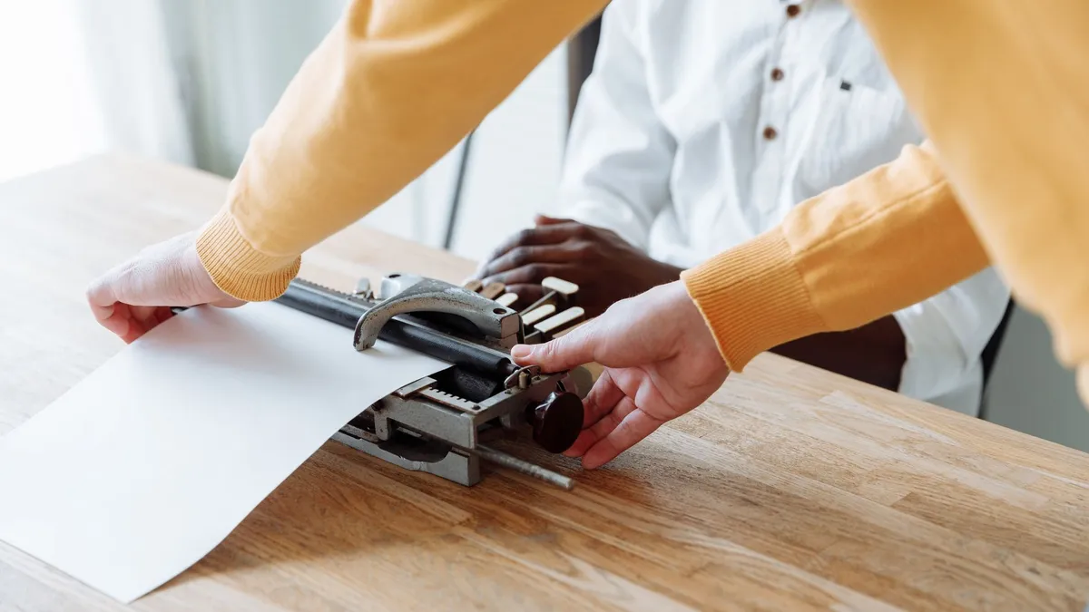 A close-up of hands using a braille typewriter on a wooden table, emphasizing accessibility.