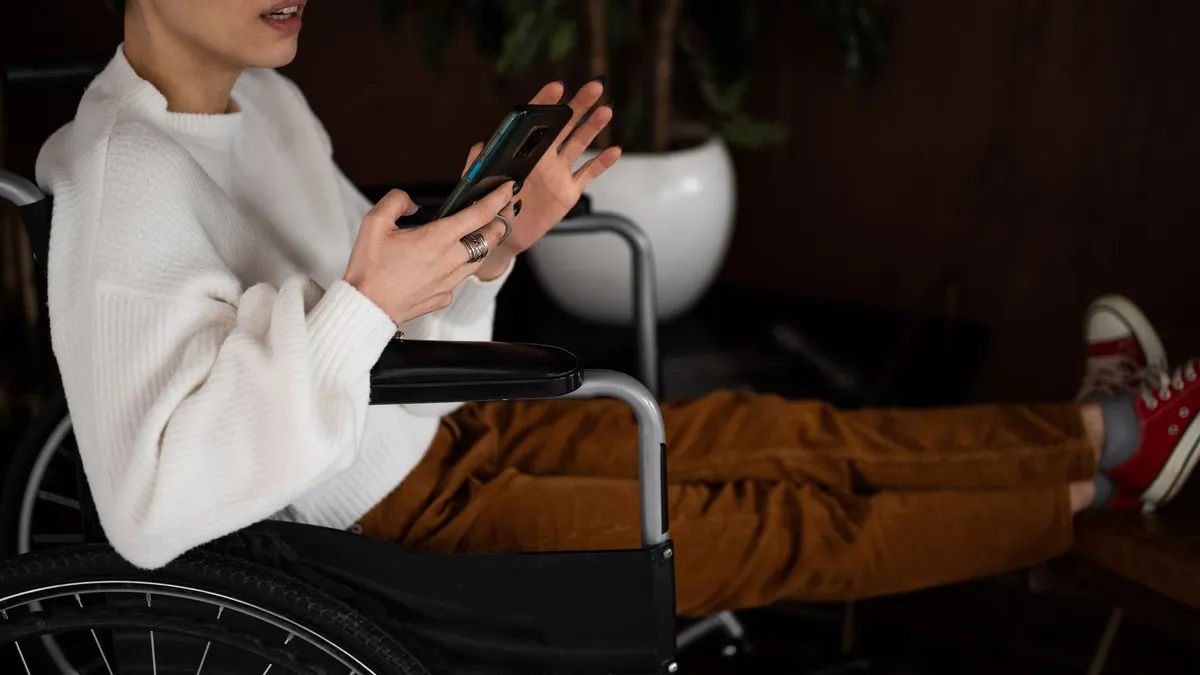 Side view of crop unrecognizable female millennial with disability sitting in wheelchair and browsing mobile phone