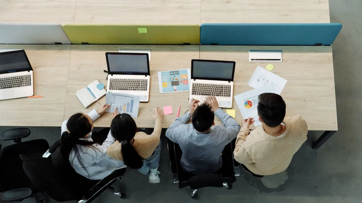Aerial view of four colleagues working with laptops and documents at a shared desk.