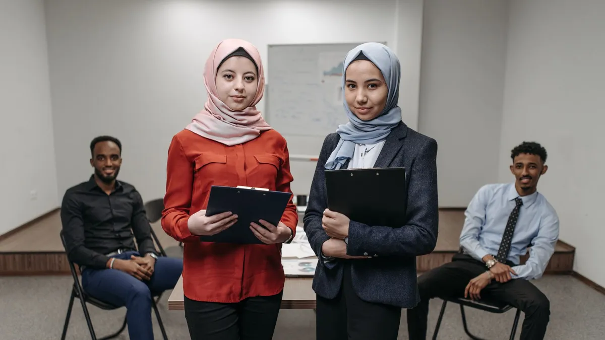 Two women in hijabs and two men having a business meeting in an office setting.