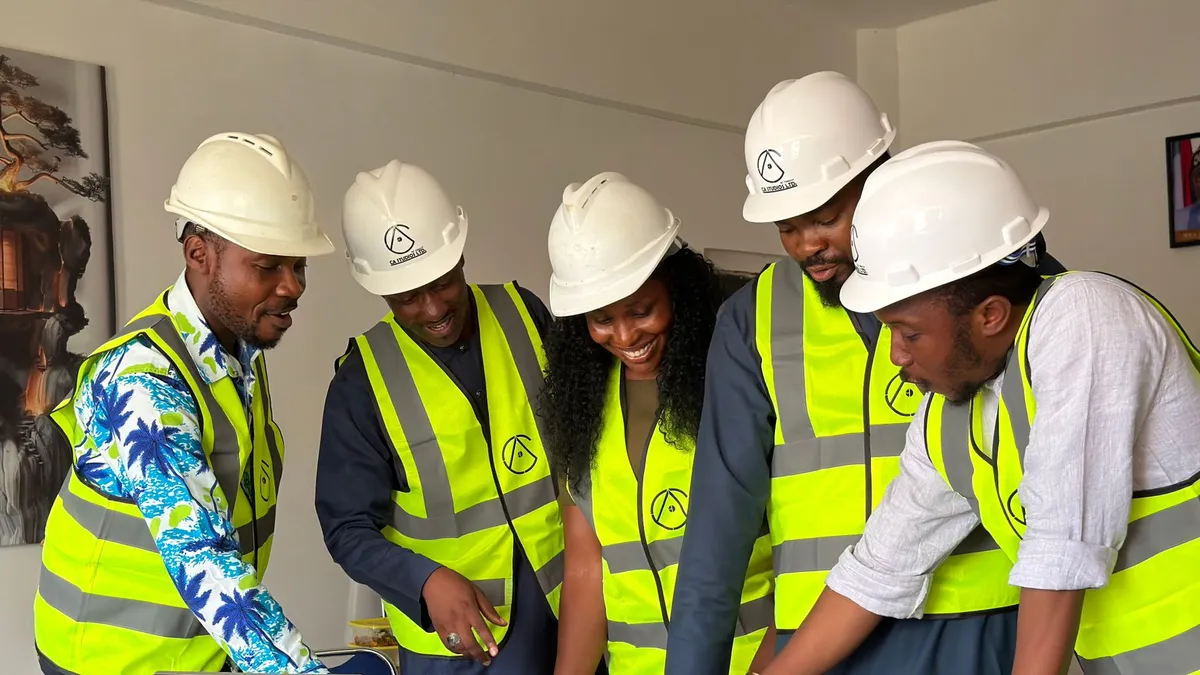 Group of engineers in hard hats and safety vests reviewing blueprints in an office setting.