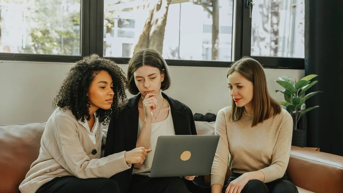 Three women working together on a laptop indoors. Teamwork and collaboration.