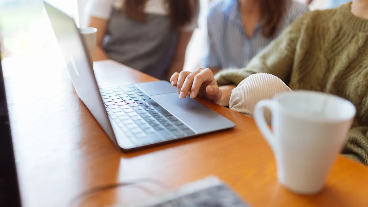 Group of women collaborating in a workspace with a laptop and coffee mugs on the table.