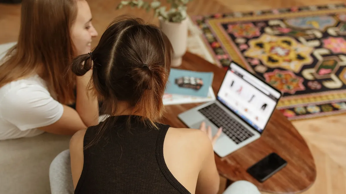 Two women engaged in online shopping sitting at home with a laptop and cozy decor.