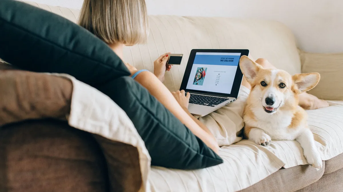 A woman using a laptop for online shopping with her corgi dog beside her on the couch.