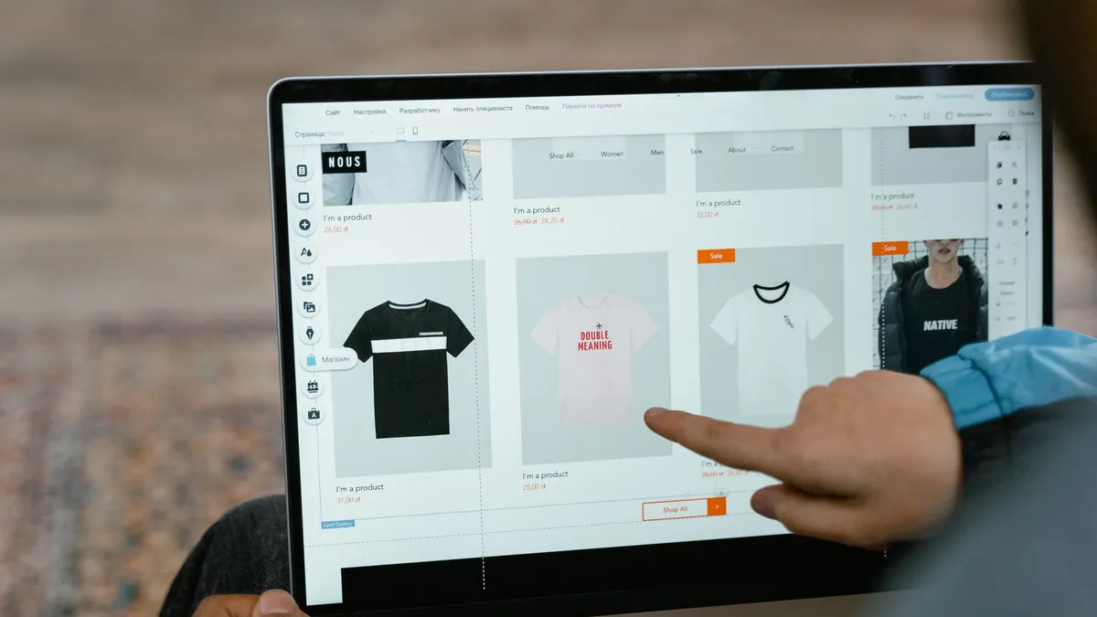 A person points to t-shirt options in an online store on a laptop screen.