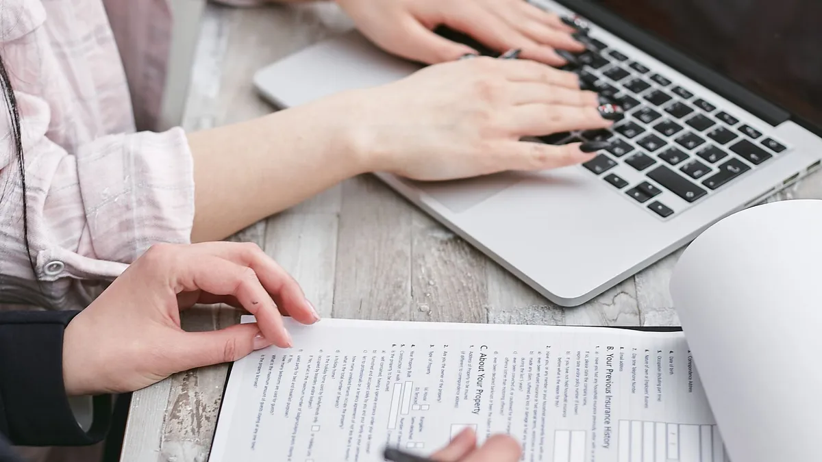 Close-up of hands typing on a laptop and reviewing business documents, focused on finance and legal tasks.