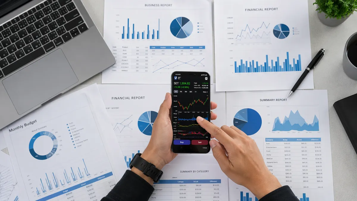 Business person reviews financial data and graphs on a mobile device surrounded by reports.
