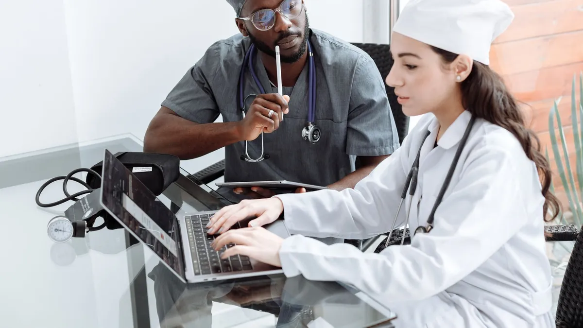 Two doctors discuss patient diagnosis using laptop in hospital office.