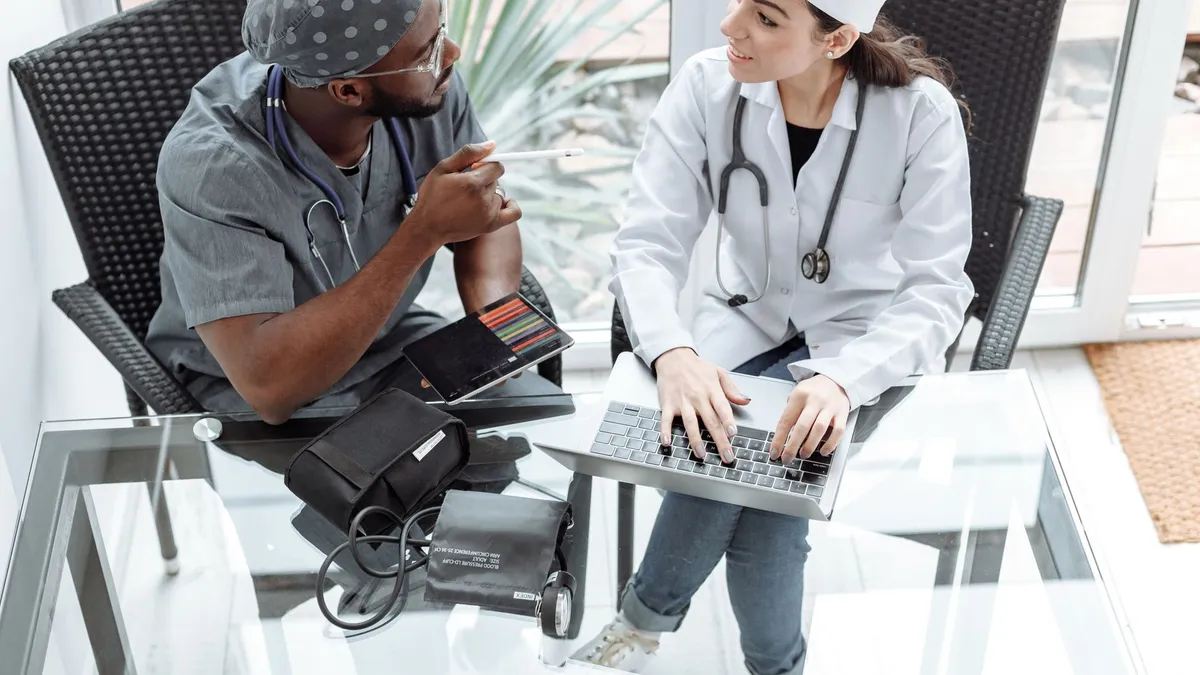 Two doctors discussing patient care using a laptop and tablet indoors.