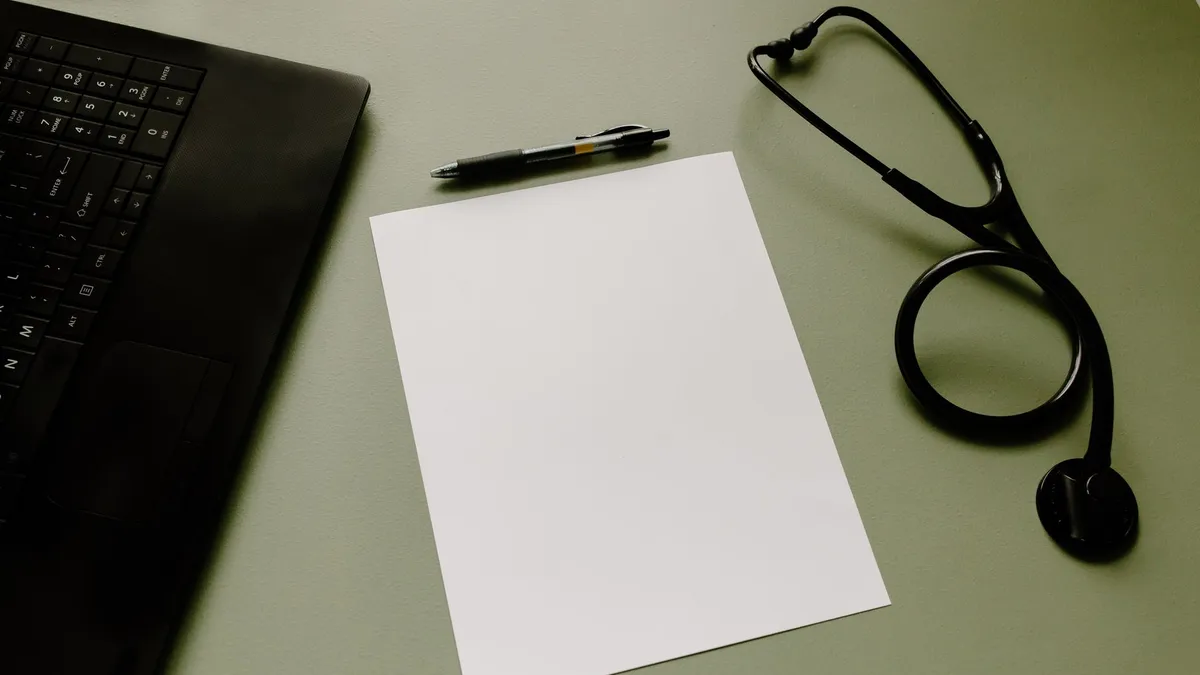 Professional workspace featuring a laptop, stethoscope, pen, and paper sheet for healthcare tasks.