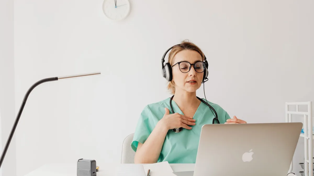 Doctor in a green scrub conducting an online video consultation using a laptop and headphones.