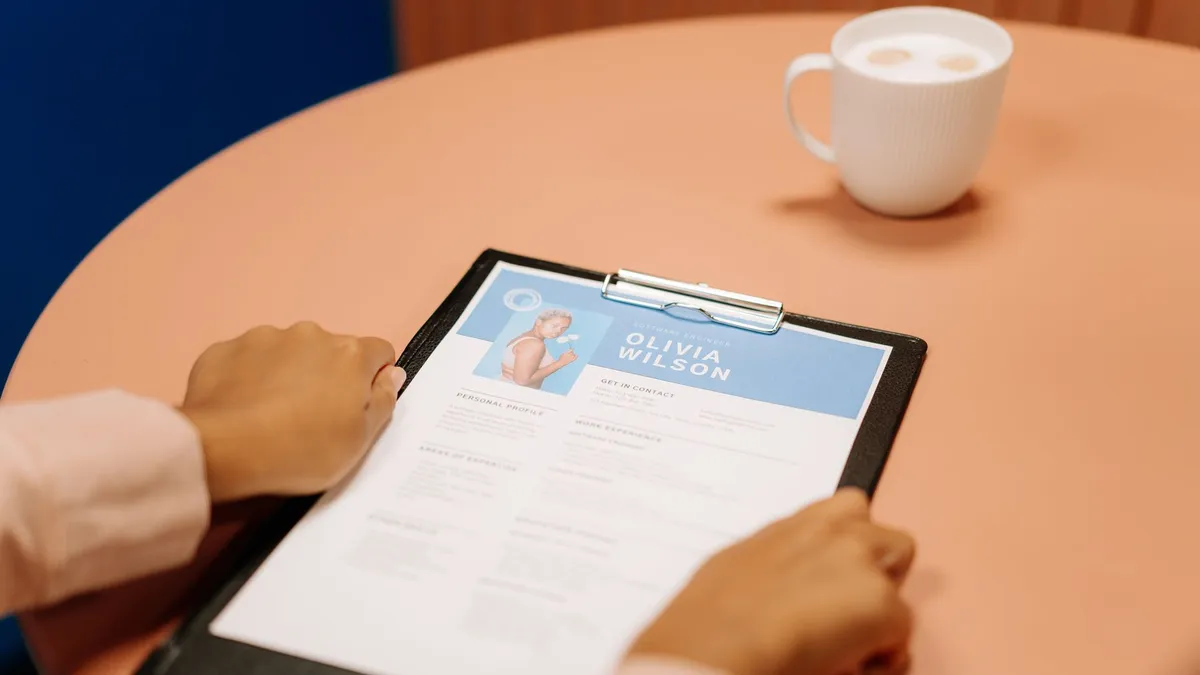 Close-up of hands holding resume during interview with coffee on table, highlighting workplace setting.
