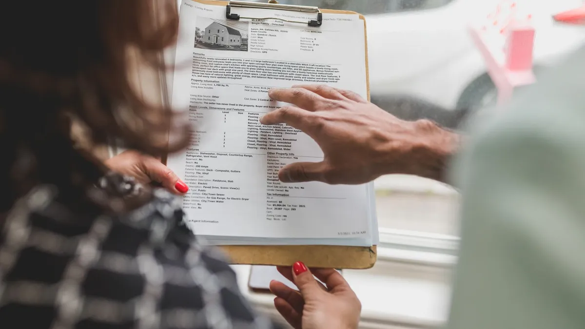 Real estate agent discussing property details with client using a clipboard indoors.