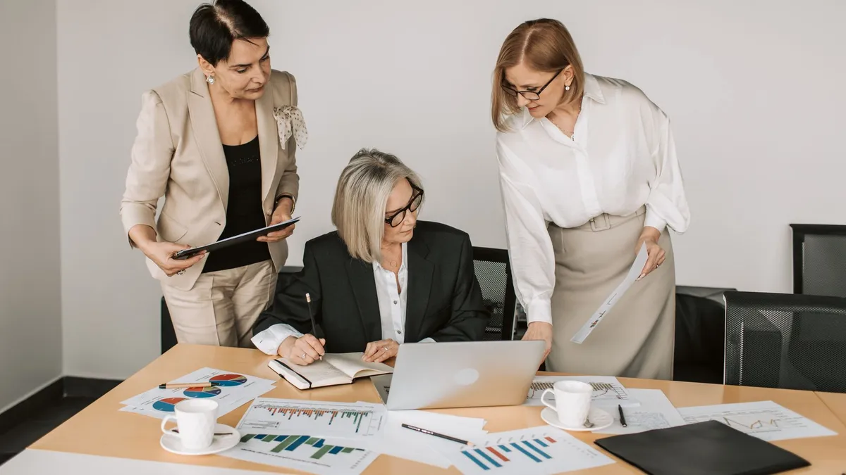 Three businesswomen discussing documents during a meeting in a modern office setting.