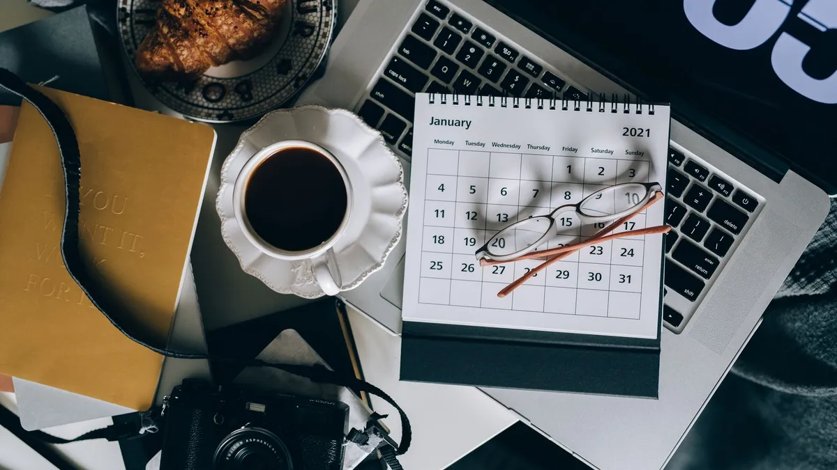A serene workspace setup with coffee, croissant, laptop, and calendar, ideal for organizing plans.