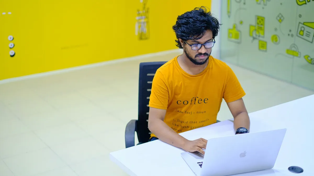 Young man wearing eyeglasses working on laptop in vibrant digital agency office.
