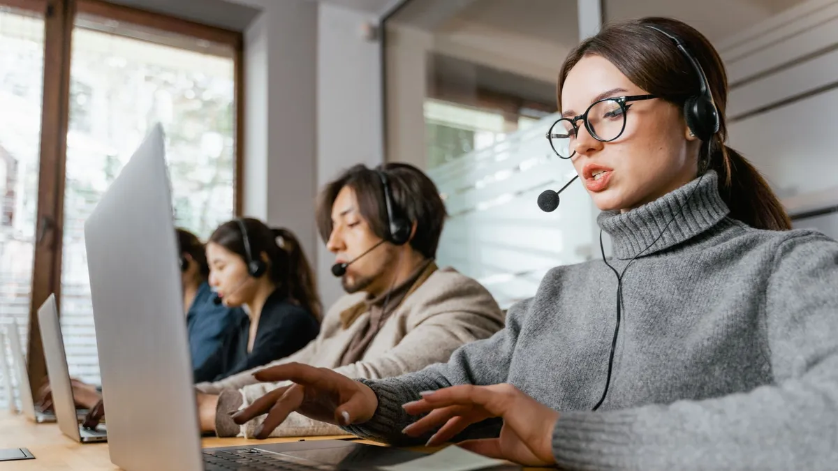 Four call center employees working with headsets and laptops in a modern office setting.