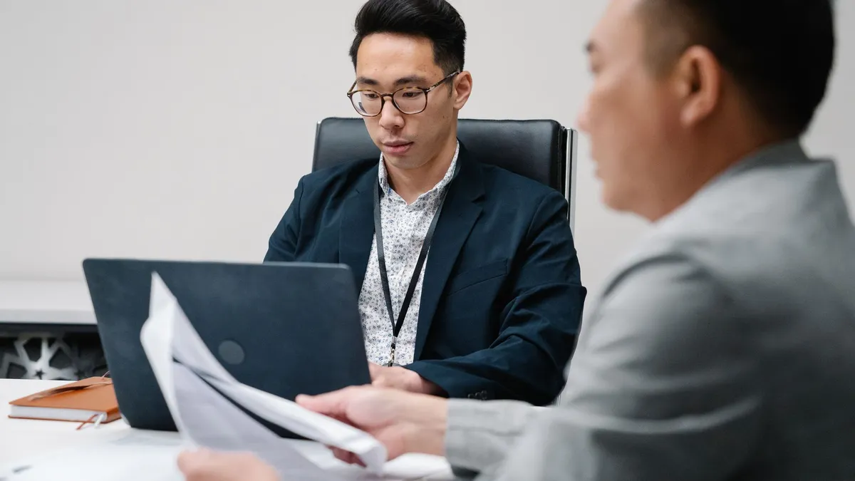 Two business professionals focused during a meeting, working on laptops and documents.