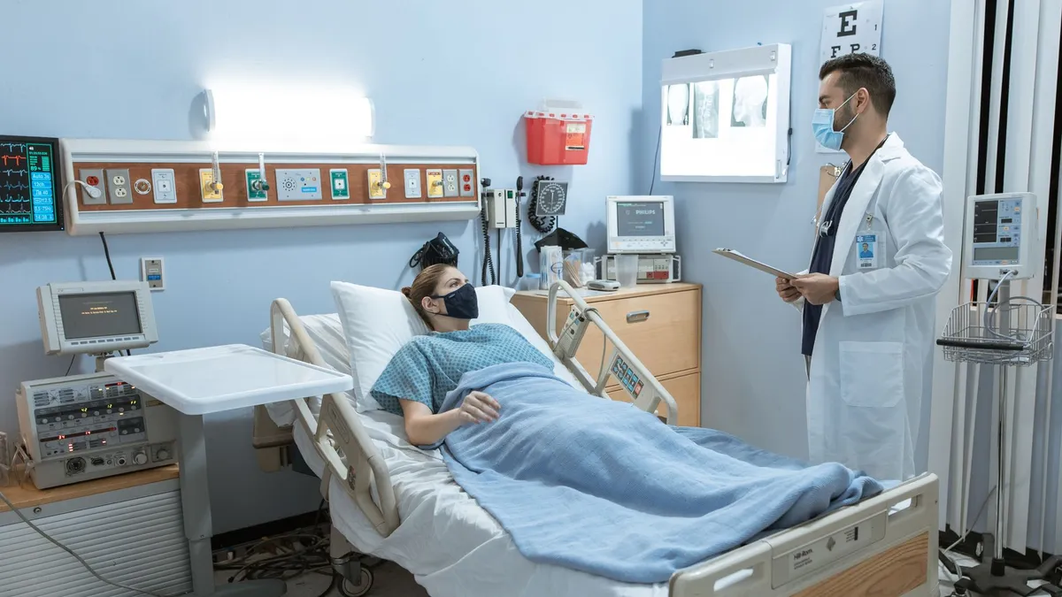 A doctor checking on a patient in a hospital room, both wearing face masks for safety.