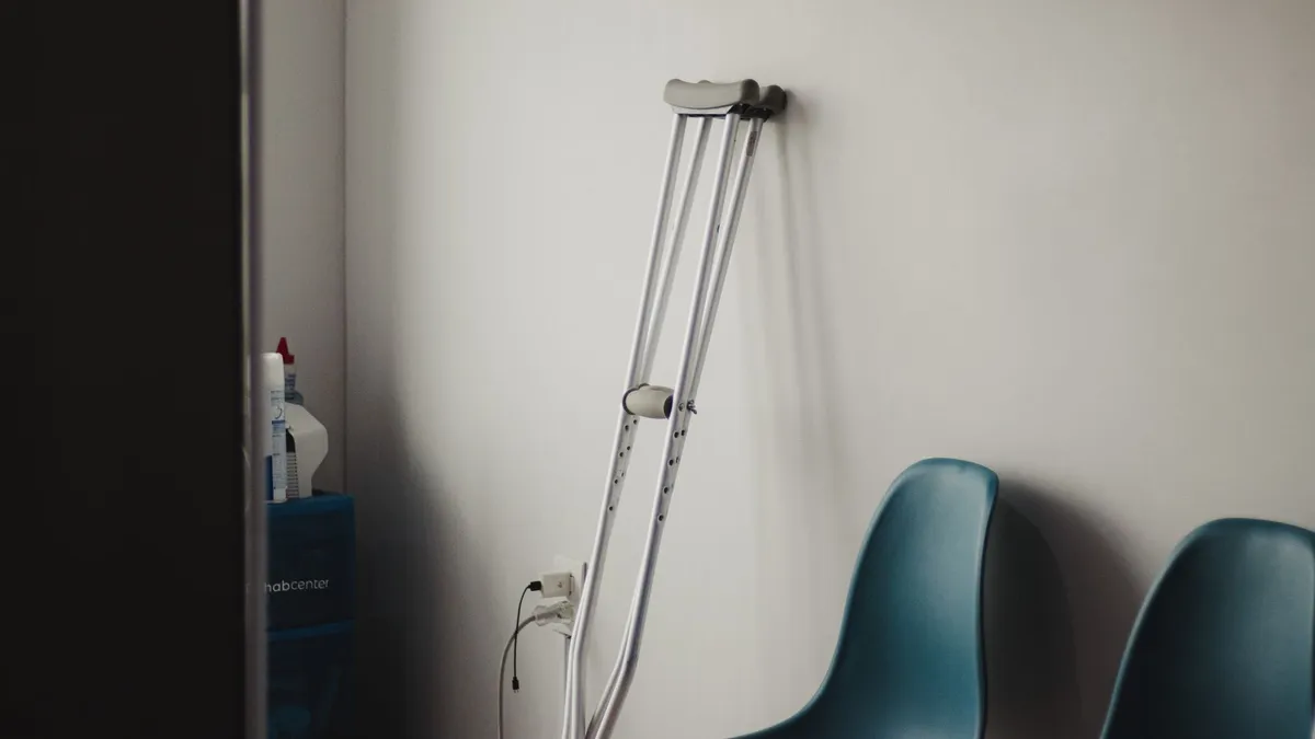 Crutches resting against a wall in a minimalist waiting room with blue chairs.