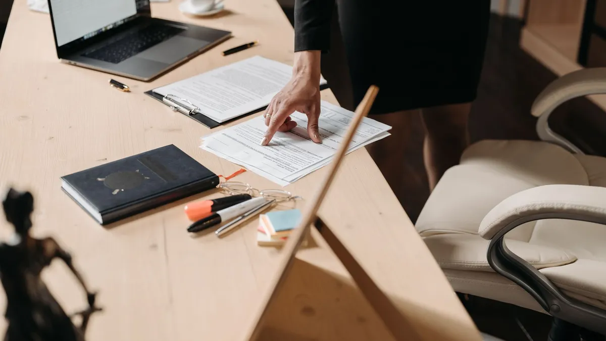 Businesswoman pointing at paperwork on a desk in an office setting, highlighting key data.