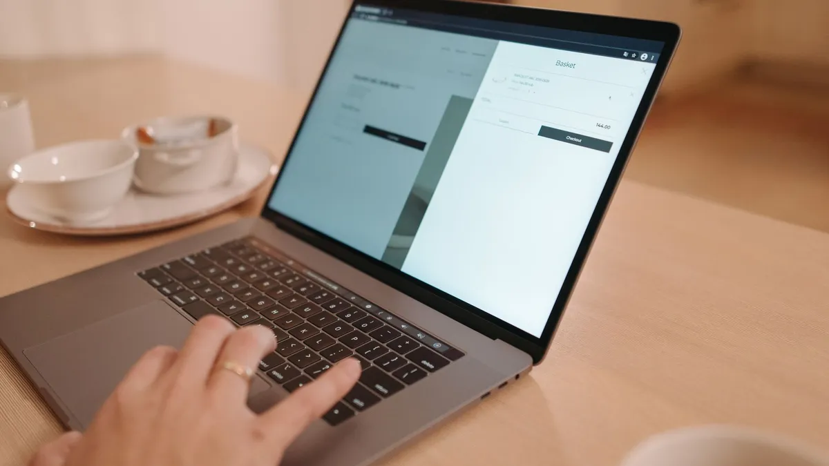 A close-up view of a person using a laptop on a wooden table indoors, creating a warm and professional atmosphere.