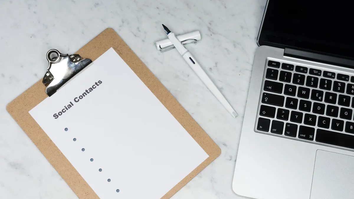 Minimalist workspace featuring a clipboard, laptop, and pen on a marble surface.