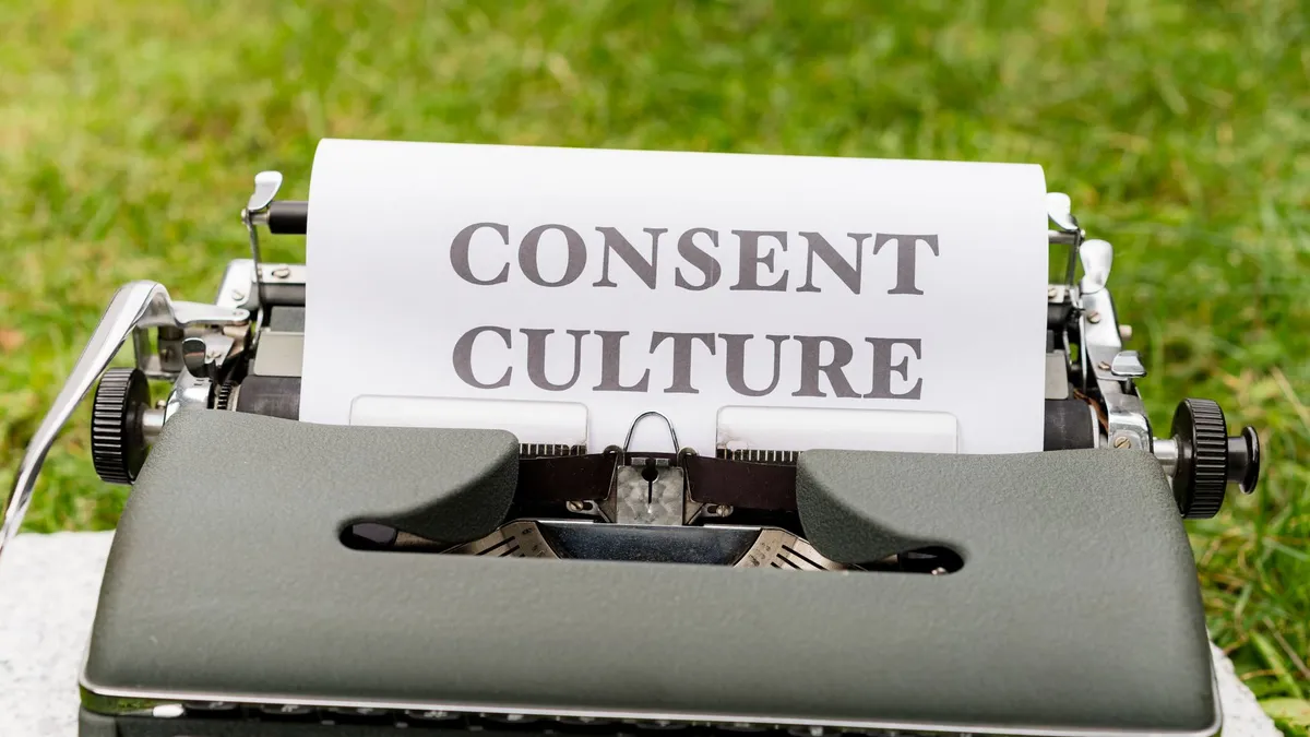 Close-up of a vintage typewriter with 'Consent Culture' typed on paper, set outdoors.