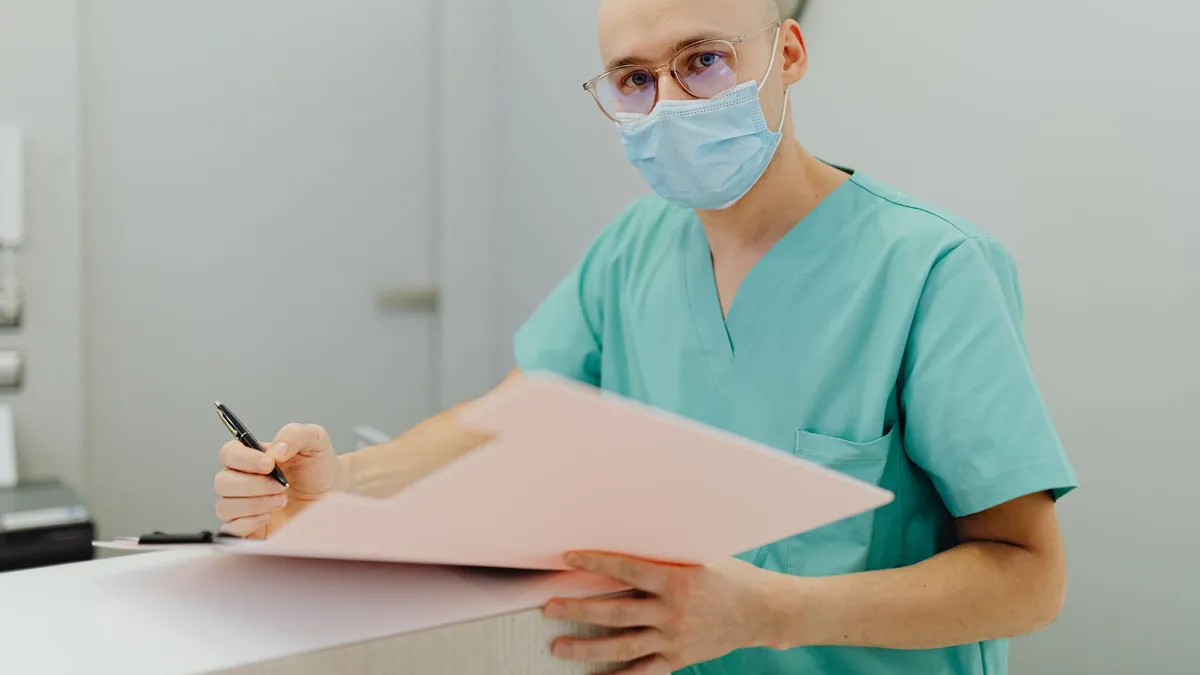 Medical professional in scrubs with mask, focusing on patient care documentation.