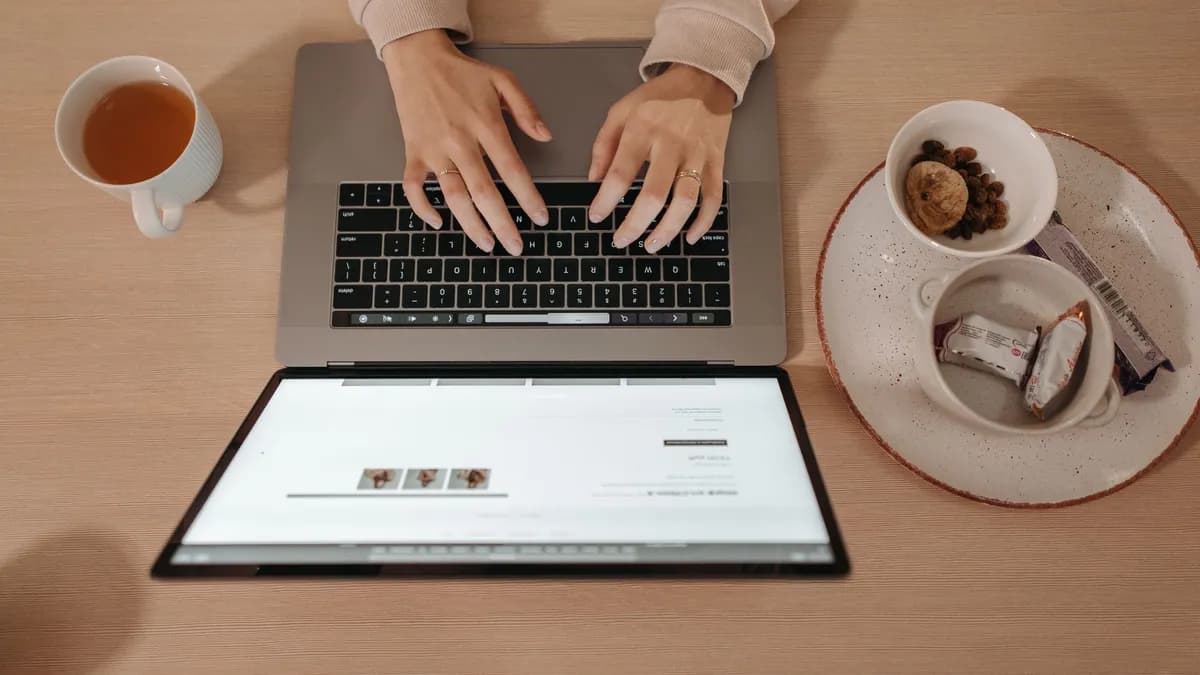Woman works on laptop with tea and snacks, showing work-from-home setup.