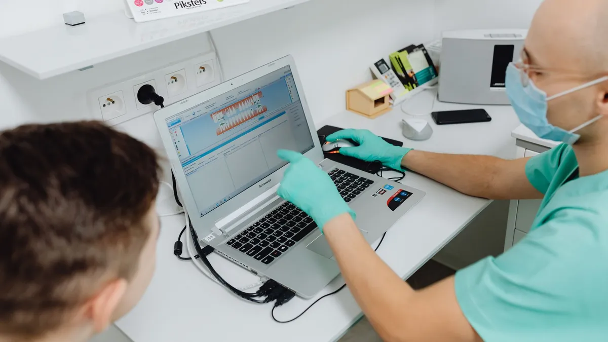 Dentist explaining dental diagnosis to a patient using a laptop in a modern clinic.