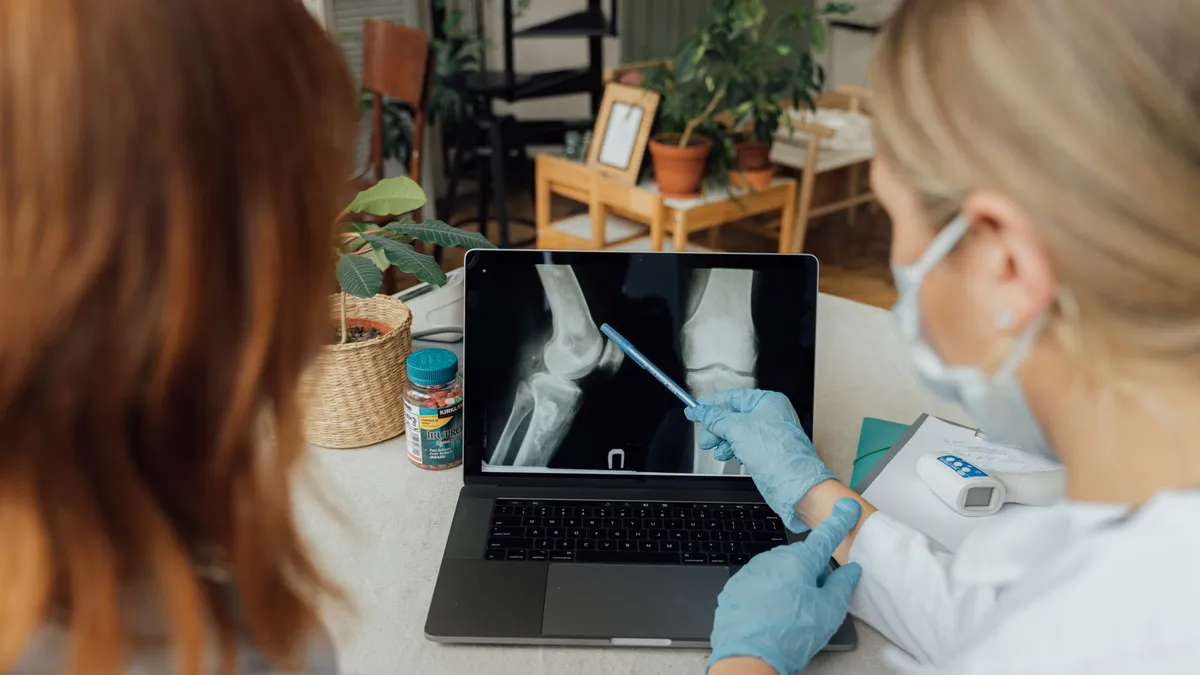 Two healthcare workers in a consultation reviewing x-ray images on a laptop.