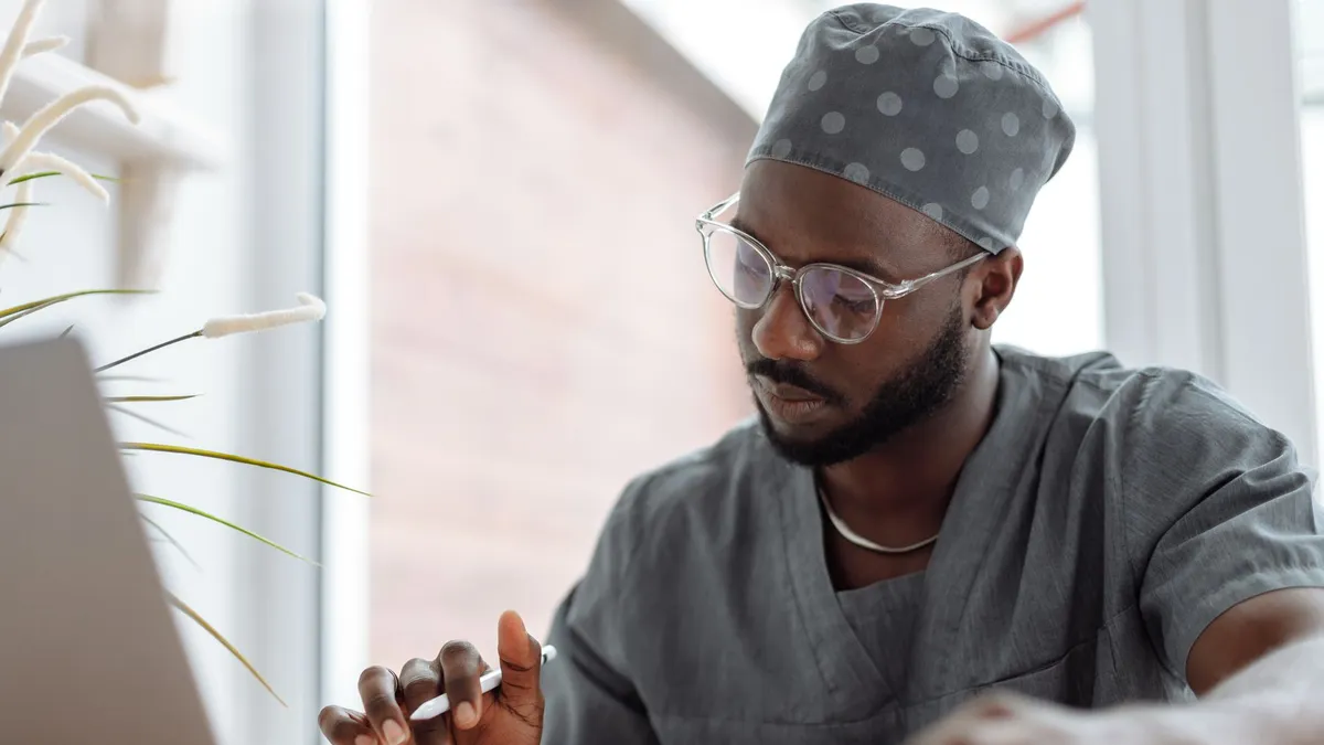 A focused male doctor in scrubs working on a laptop, showcasing professionalism and modern healthcare technology.