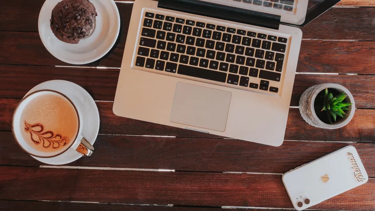 Top view of a cozy workspace featuring a laptop, coffee, and succulent on a wooden table.