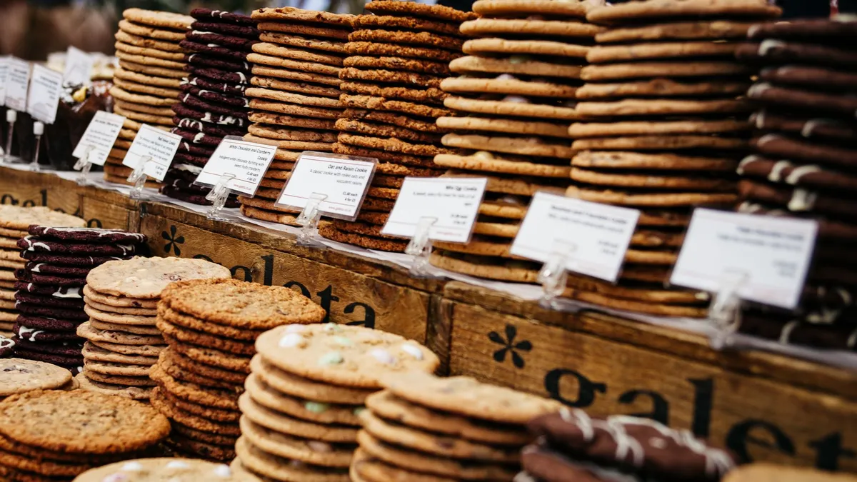 Assorted cookies elegantly stacked and labeled at a bustling market stall.