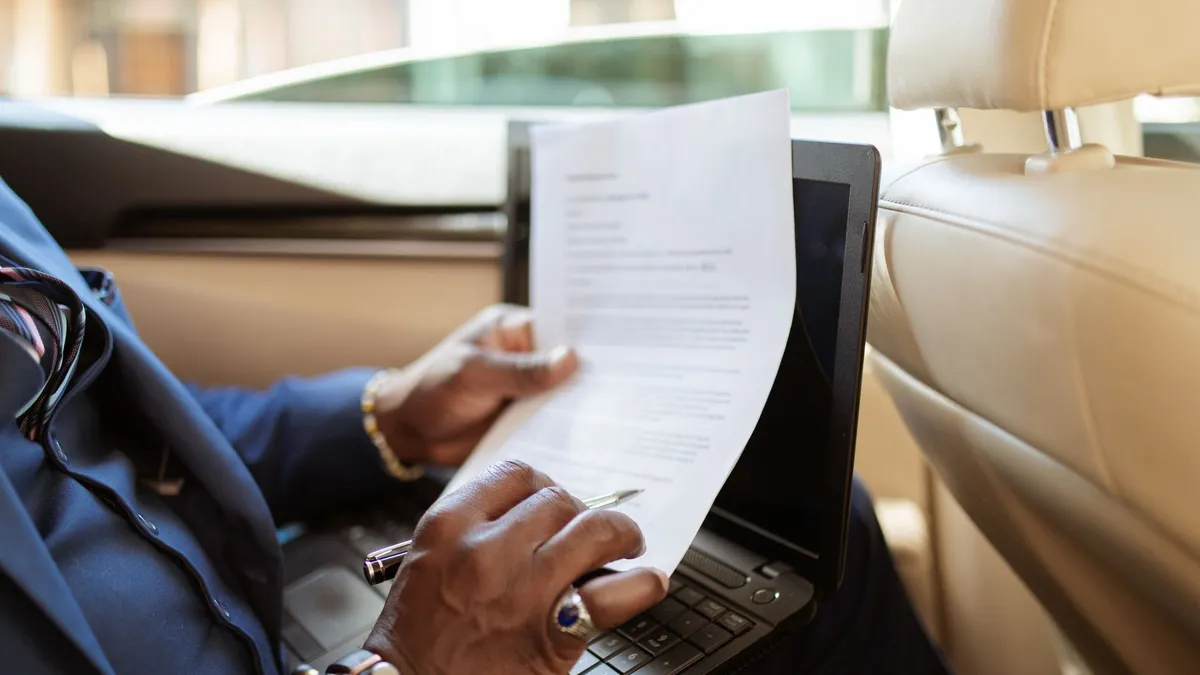 A businessman reviews documents on a laptop while traveling in the backseat of a car.