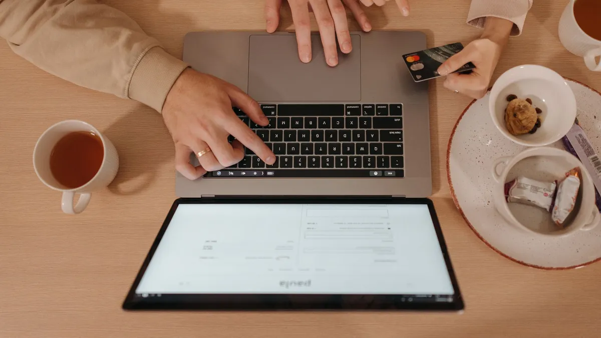 Two people using a laptop for online shopping with a credit card, seen from above.