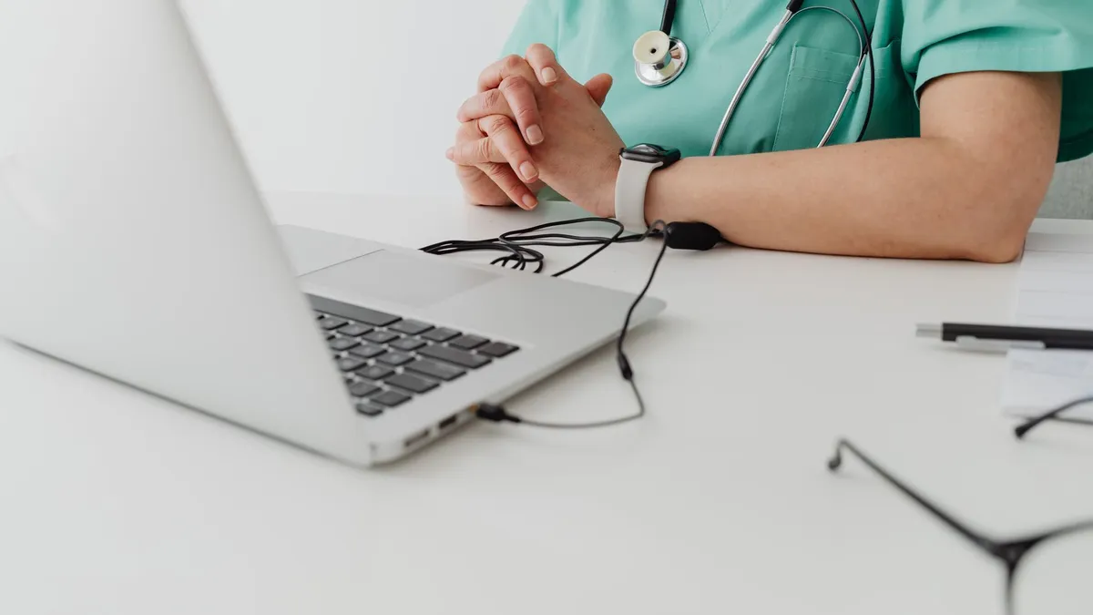 Medical practitioner in scrub suit using a laptop for remote consultation and documentation.