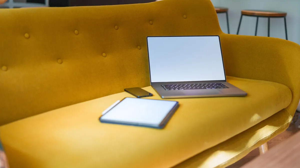 A modern living room featuring a yellow sofa with a laptop, tablet, and smartphone.