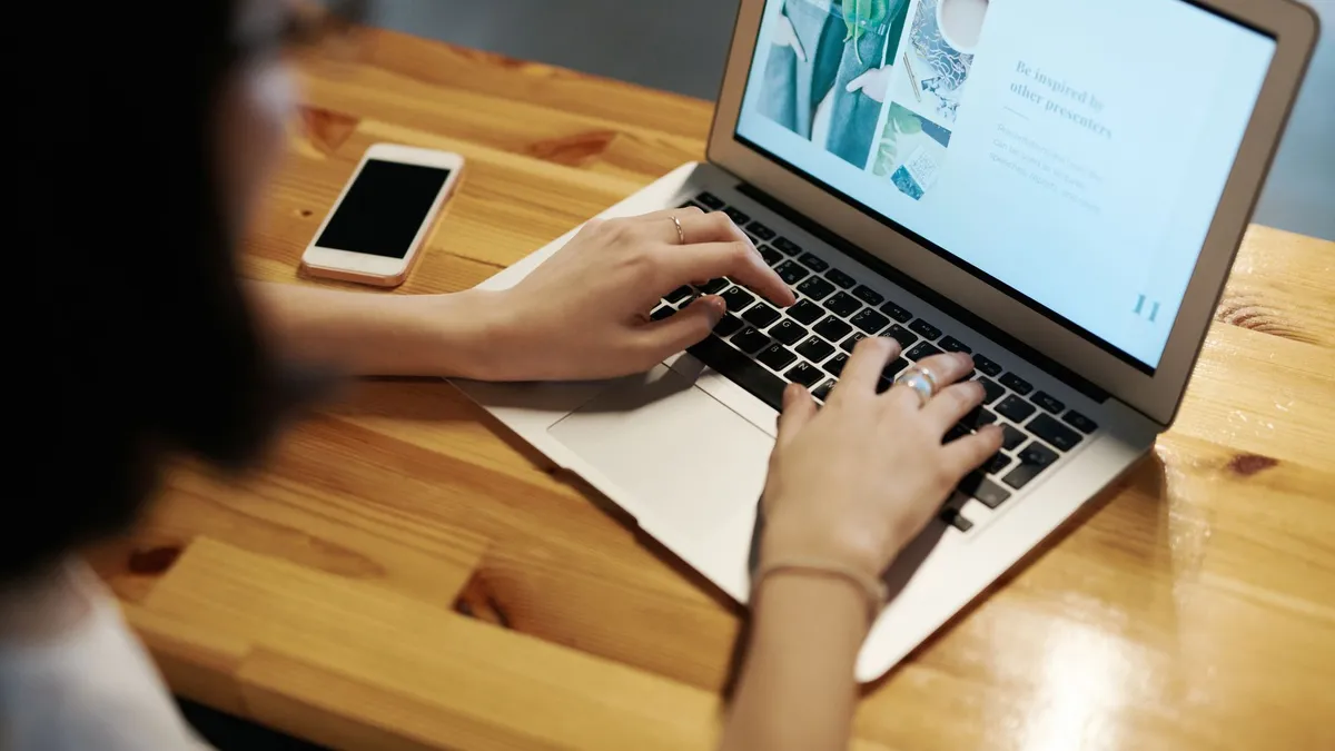 Person typing on a laptop at a wooden table with a smartphone nearby, illustrating remote work.