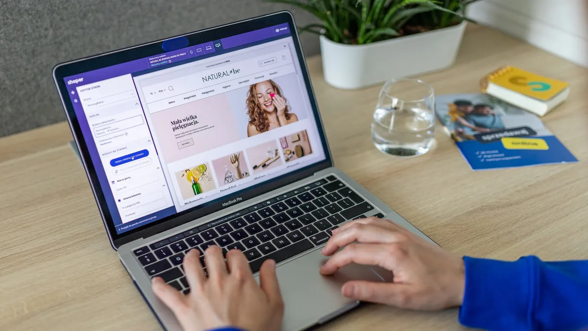 Hands typing on a laptop showing an e-commerce website in a modern office setting.