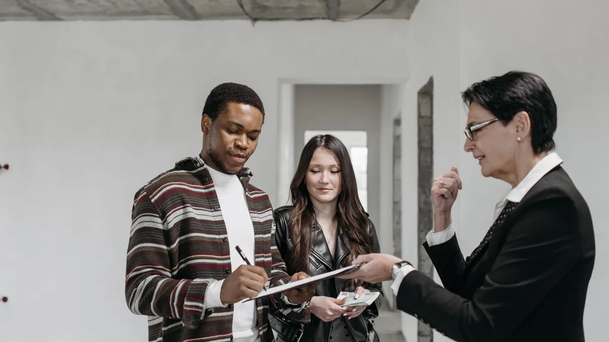 A diverse couple signing documents with a realtor in a new home setting.
