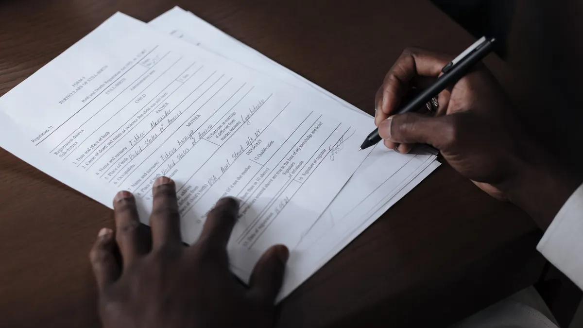 A detailed view of a man signing official documents with a pen at a table.