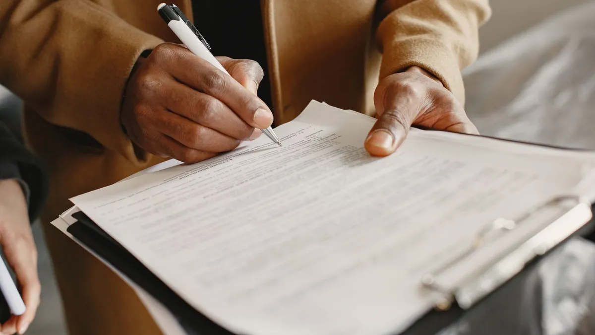 Close-up of a person signing a contract on a clipboard, focusing on legal formalities.