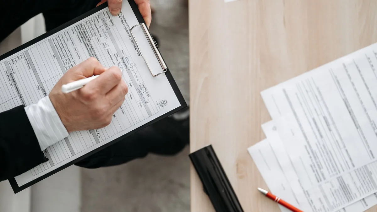 High-angle view of a person filling out forms on a clipboard, emphasizing paperwork and documentation.