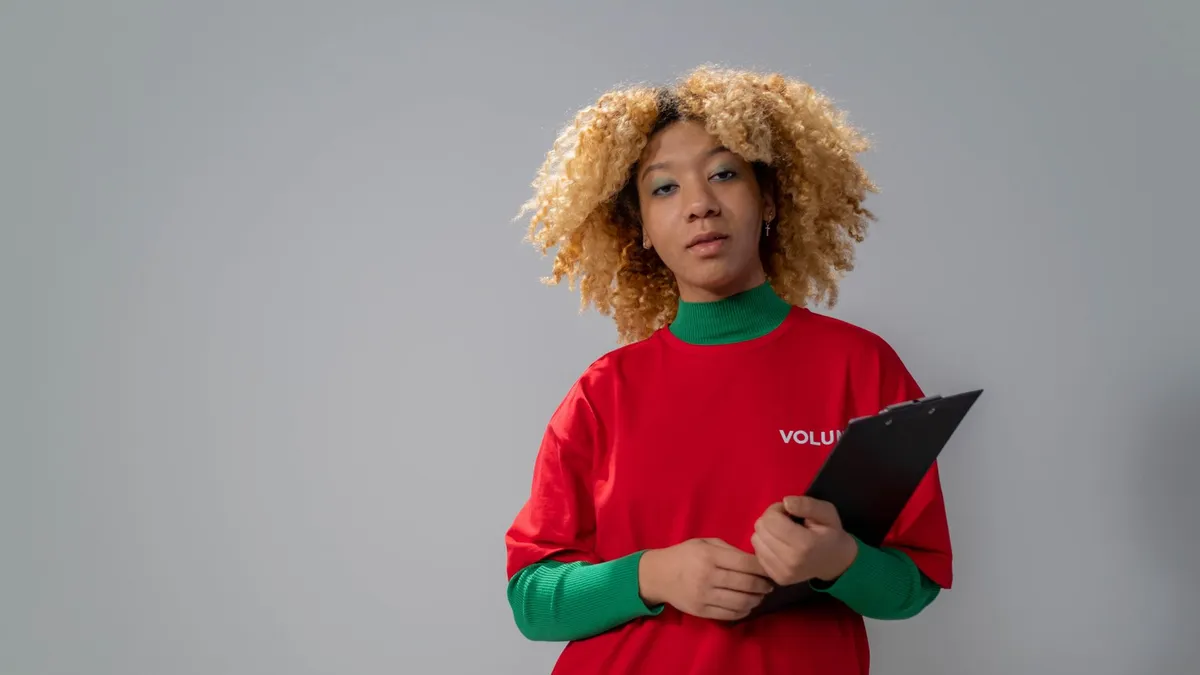 Portrait of a confident volunteer holding a clipboard in a studio setting with a neutral gray background.