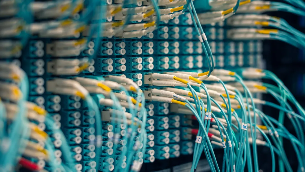Closeup of rows of tiny round white electrical connectors and long thin blue wires in data center