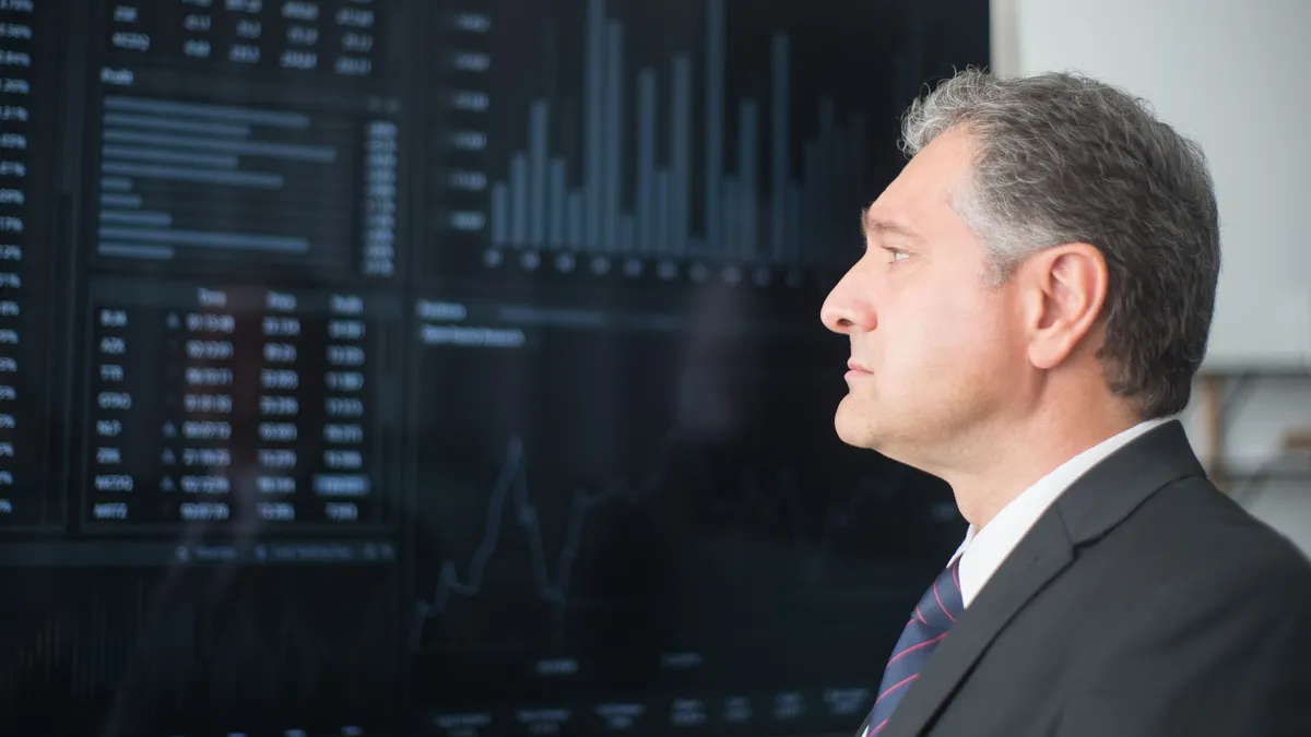 Mature businessman in corporate attire analyzing financial charts on a screen indoors.