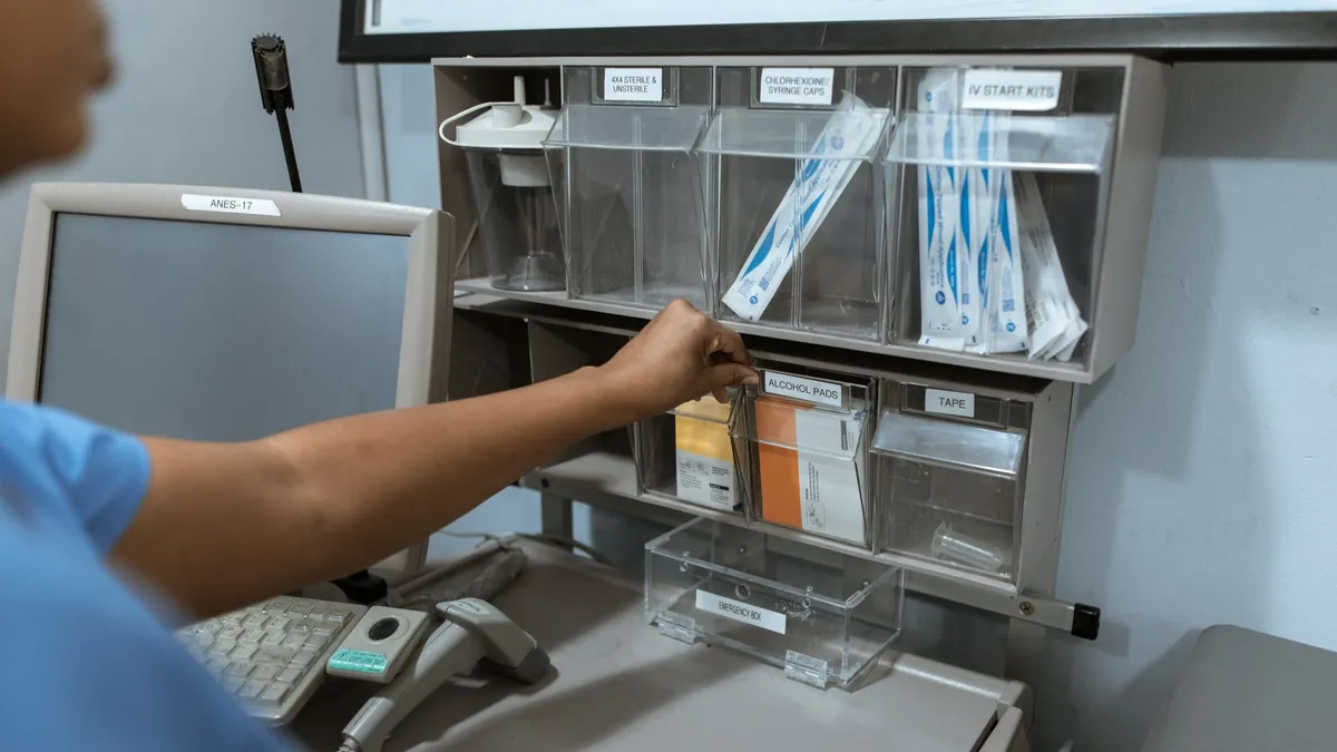 A healthcare worker organizes medical supplies in a clinic room, focusing on efficient storage.